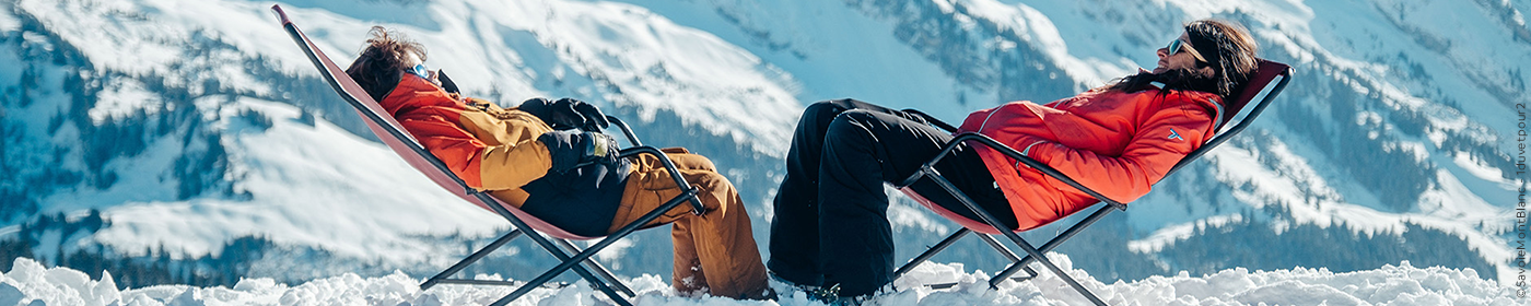 man en vrouw op een besneeuwde berg onderuitgezakt op een ligbedje naar elkaar toegekeerd