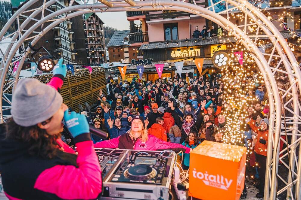 Pratende dj vanuit podium onder metalen boog naar feestende jongeren tijdens totally feest in de sneeuw
