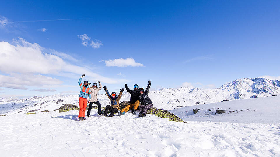 groep vrienden met handen omhoog viert wintersport op besneeuwde piste