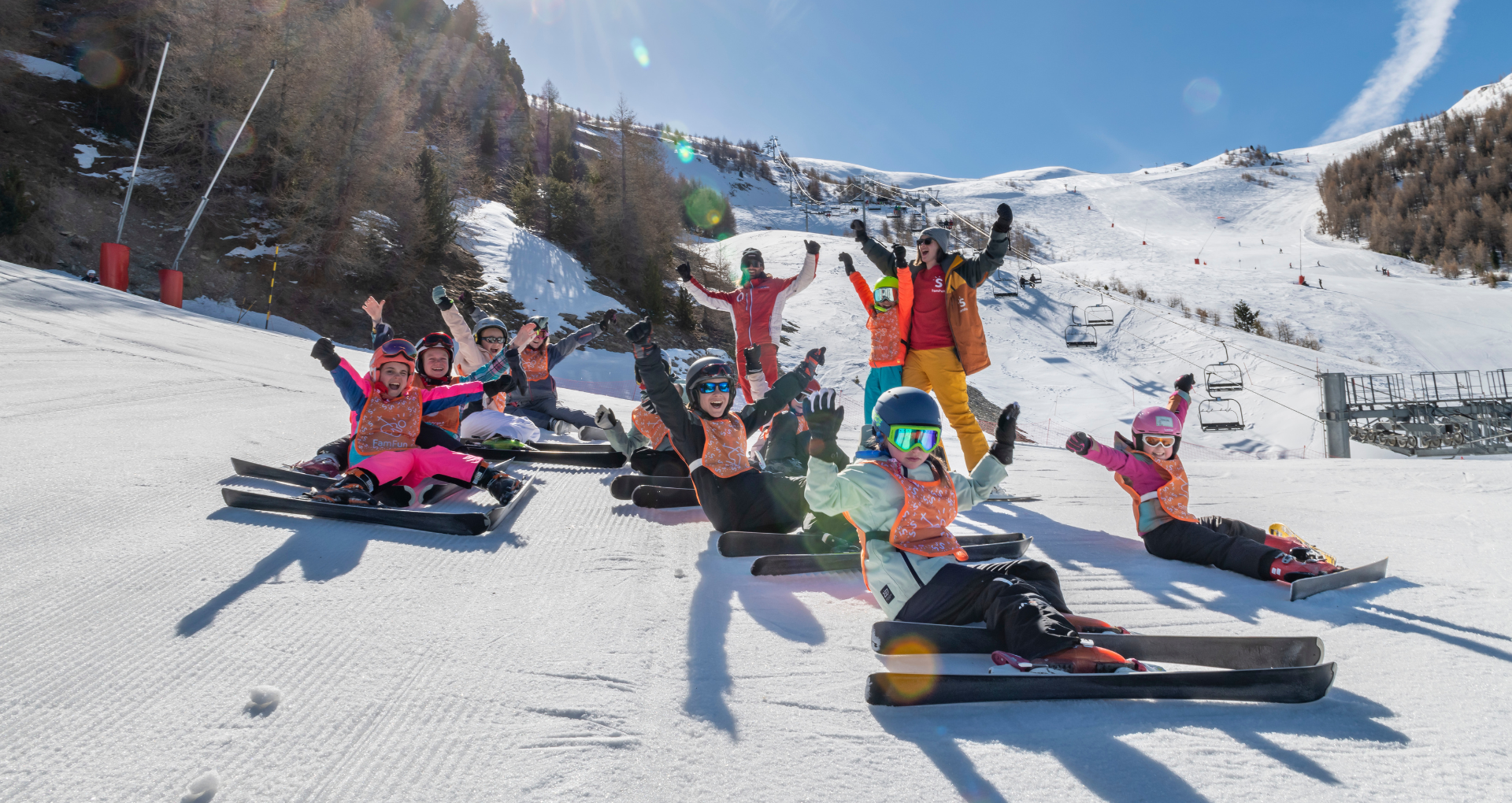 Skiklasje met handen in de lucht, zittend op skipiste tijdens famfun familievakantie met sunweb