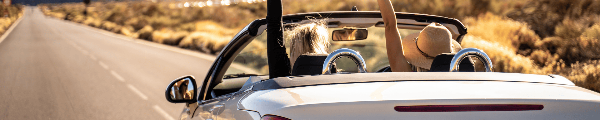 Twee vrouwen die over een weg rijden in een cabrio met hun handen in de lucht