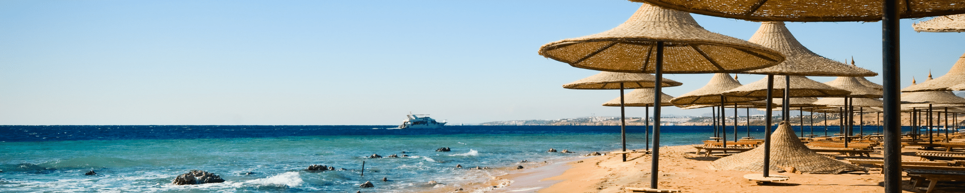 Goudgeel zandstrand met rijen parasols van gras in Sharm el Sheikh