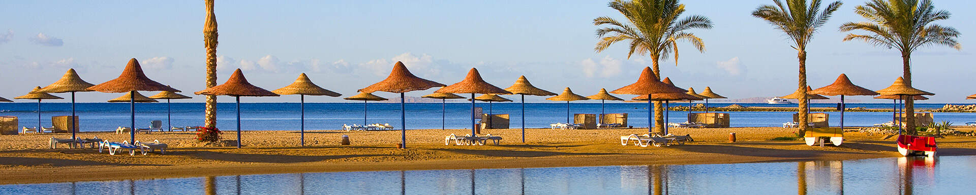 Uitzicht over kalme zee en strand met rieten parasollen, ligbedjes en palmbomen in Egypte