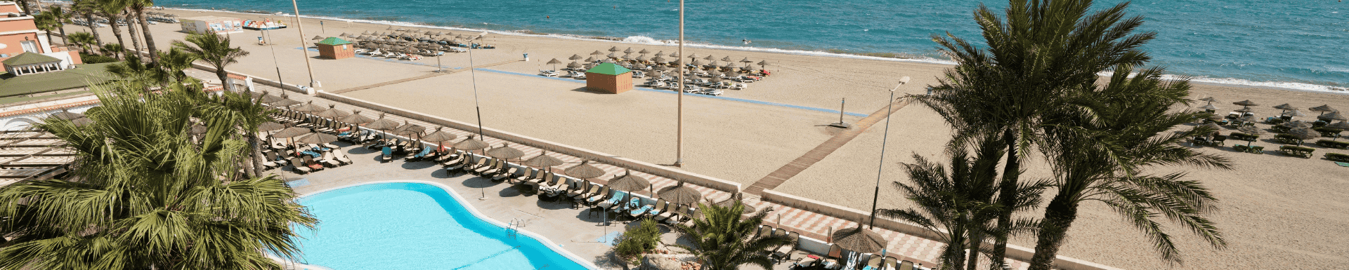 Uitzicht op een tropisch strand met een zwembad op de voorgrond, omringd door palmbomen