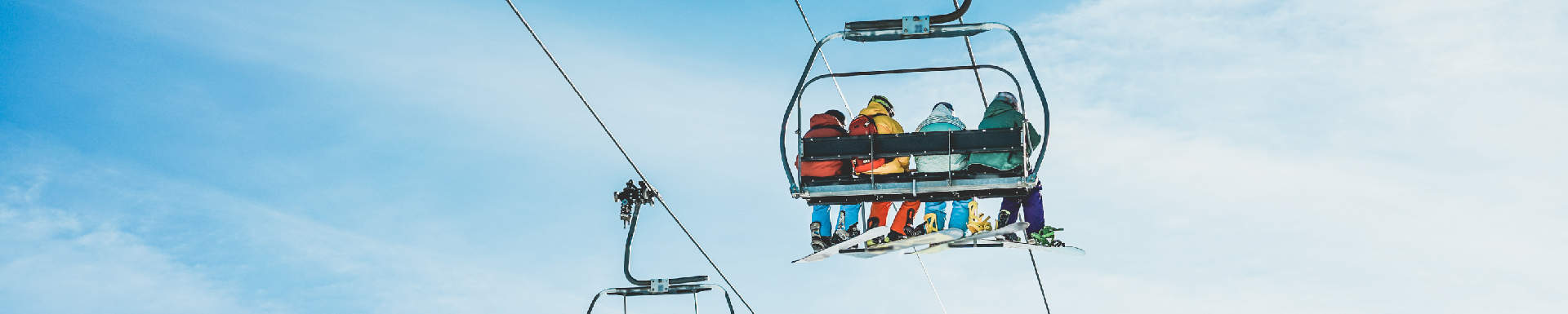 vier mensen van achteren gefotografeerd zittend in een stoeltjes skilift met skikleding aan