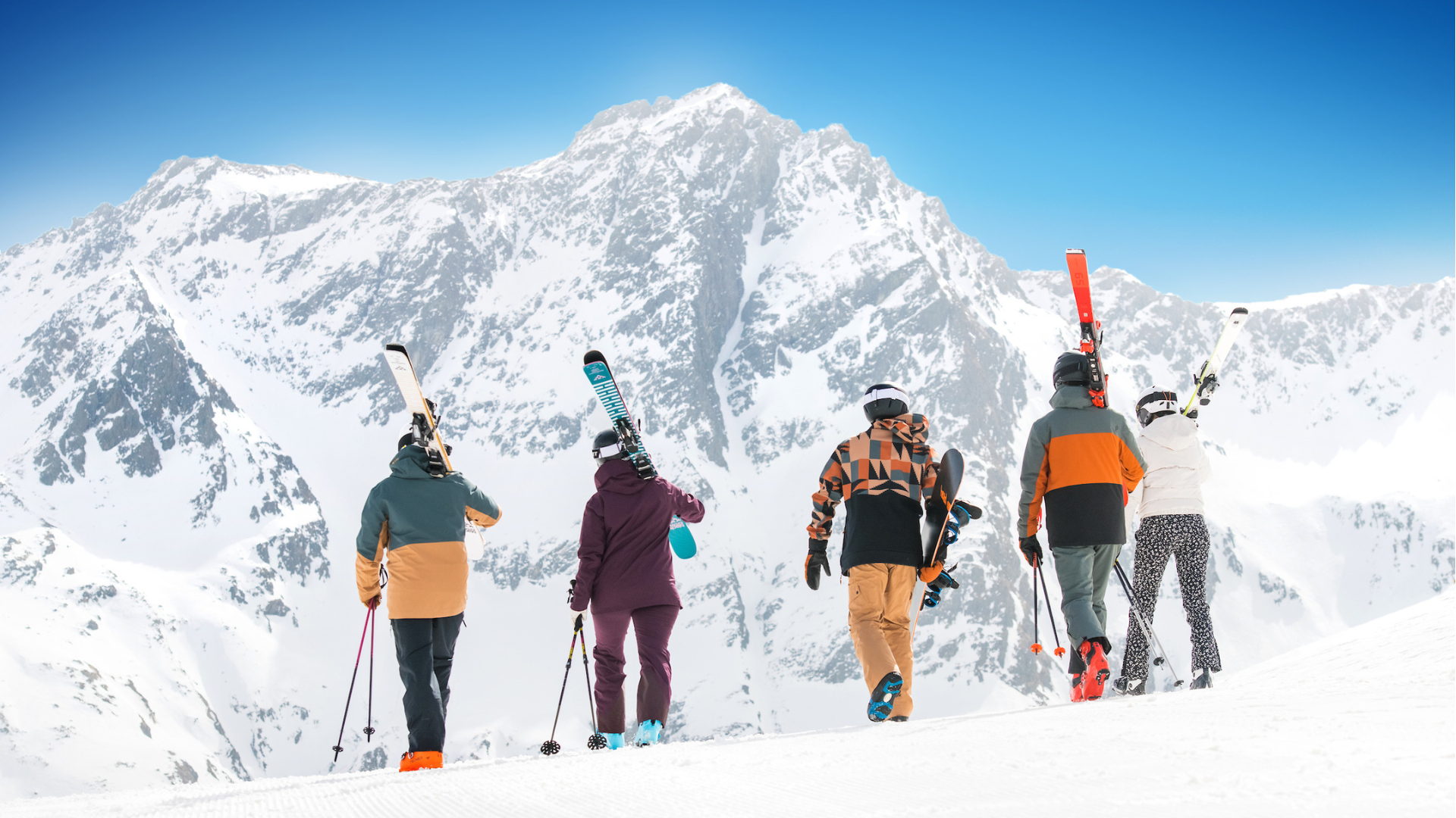 Groep skiers loopt over piste in skigebied met skies op hun schouders