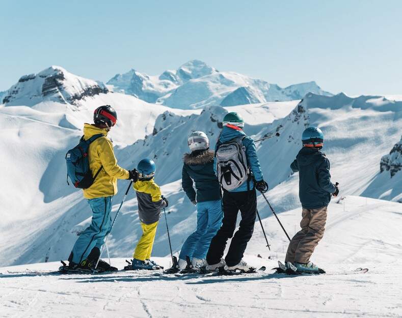 Familie op de piste uitkijkend over de besneeuwde bergtoppen