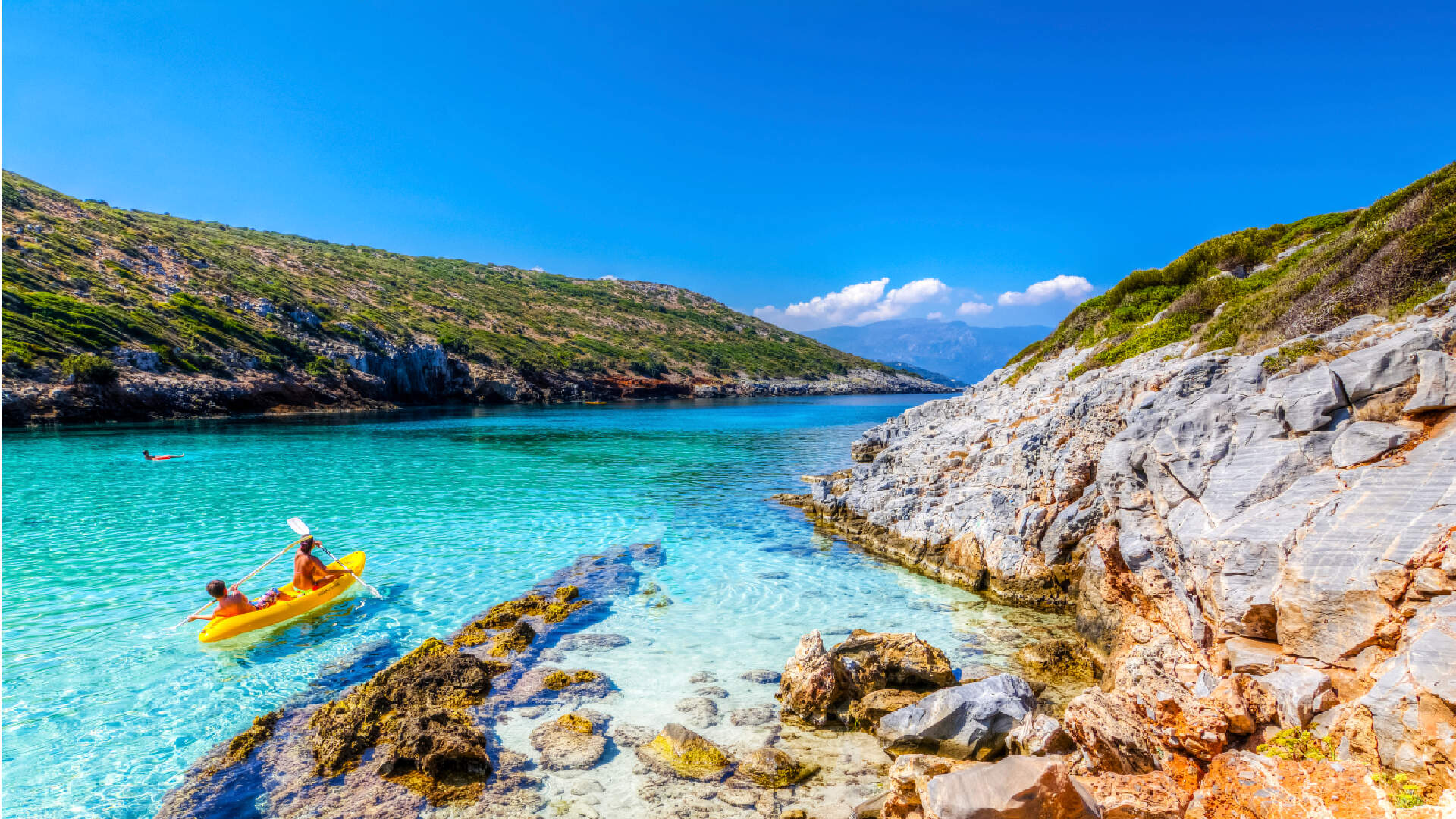 twee mensen in een gele kajak door de aquablauwe zee langs de rotsachtige kust van Samos in Griekenland