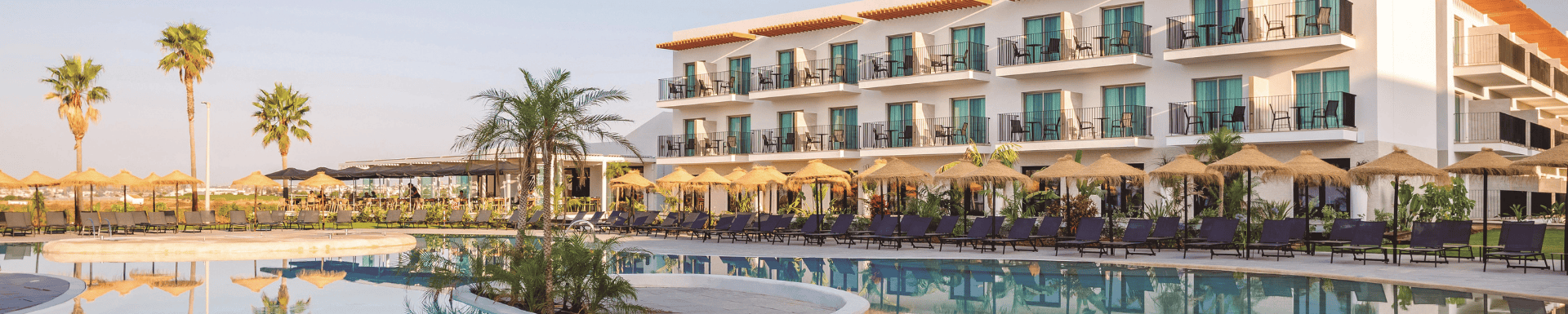 Een luxe resort met een groot zwembad omringd door ligstoelen en rieten parasols.