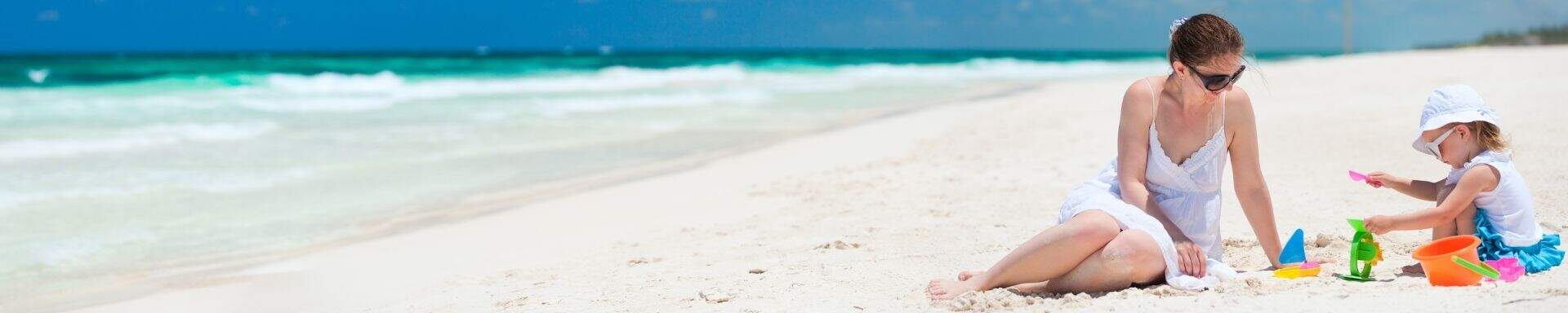 Moeder en dochter op strand met strandspeeltjes en zee op de achtergrond