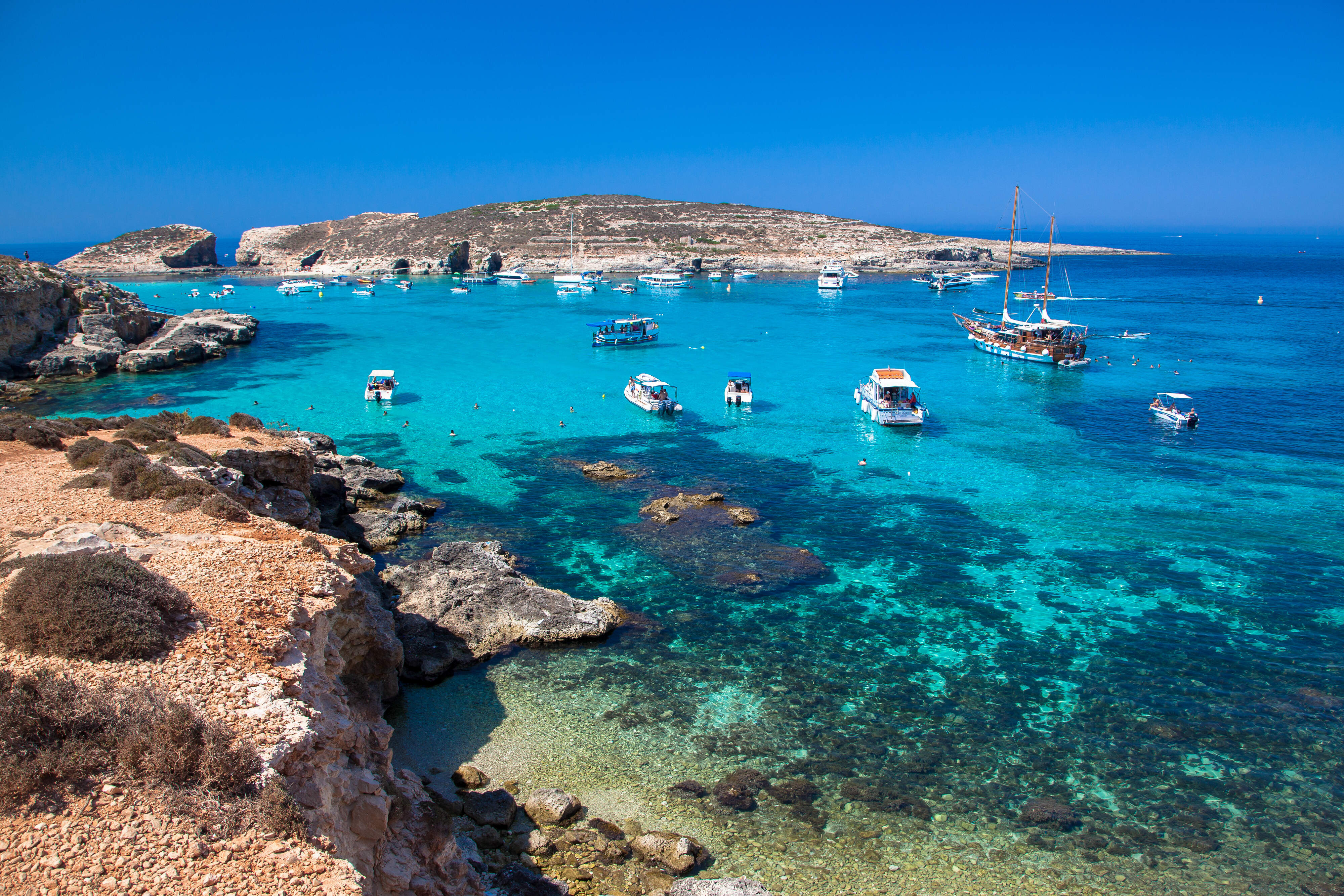 rotsachtige kustlijn met helderblauw water en bootjes op malta