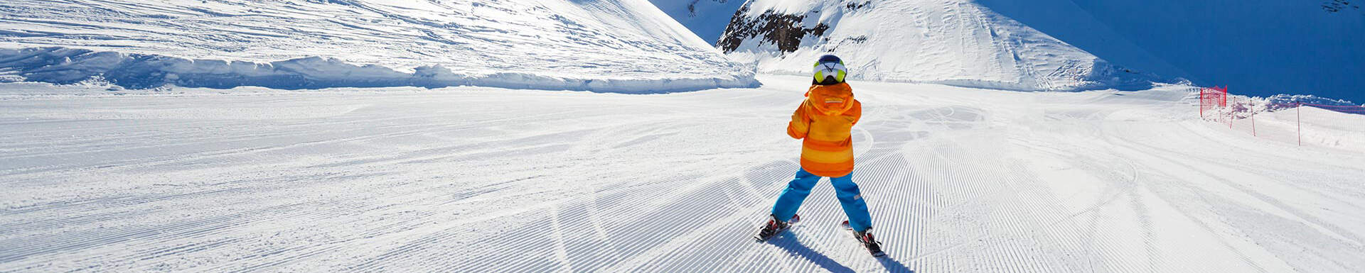 Kind in oranje-blauw pak dat van de piste skiet