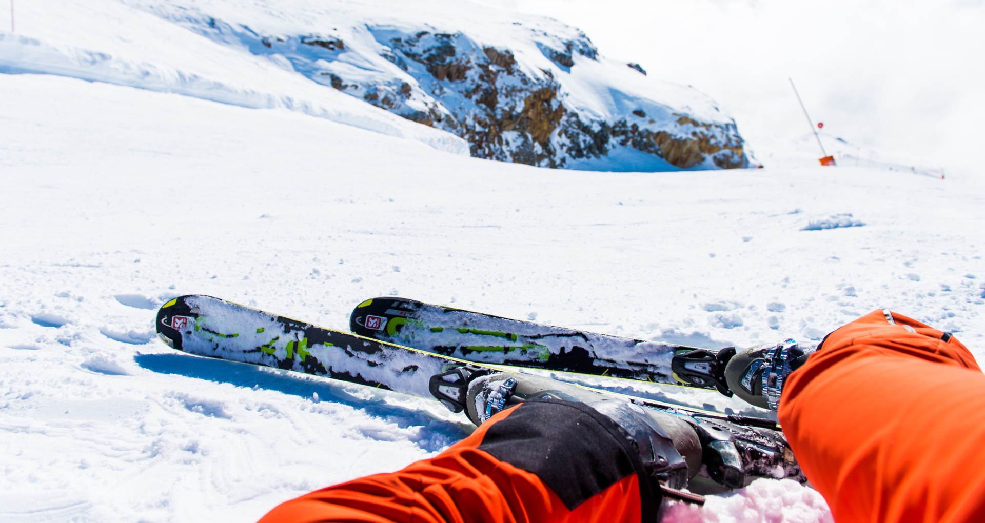 uitzicht op benen met skies in van oranje skibroek, liggend op besneeuwde piste