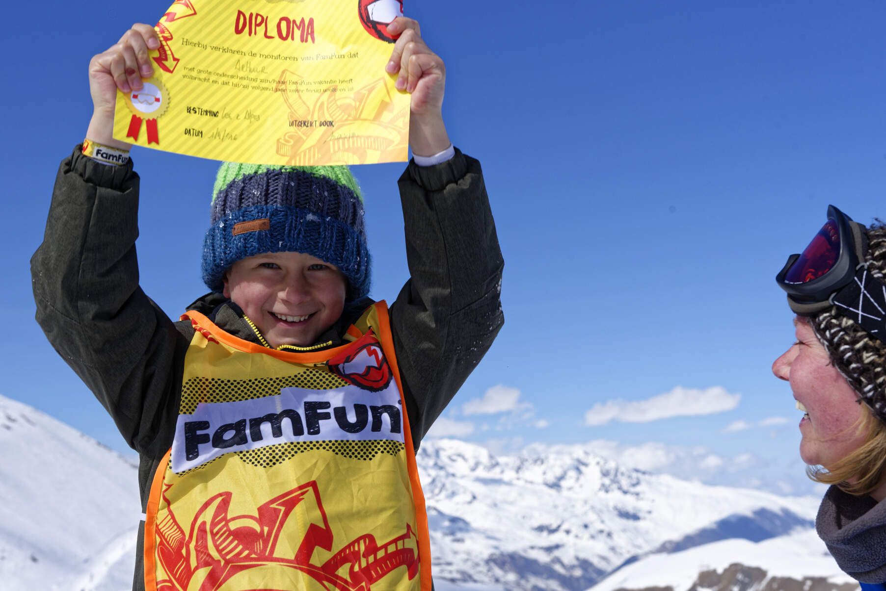 Jonge skier in besneeuwd skigebied in geel hesje houdt geel diploma trots omhoog met twee handen