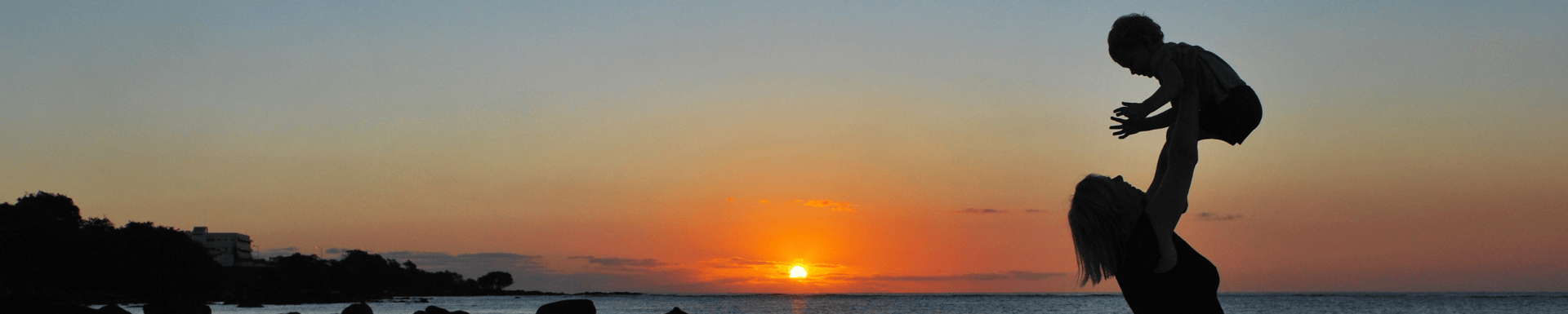 Moeder tilt haar kind omhoog tijdens zonsondergang met uitzicht over de zee