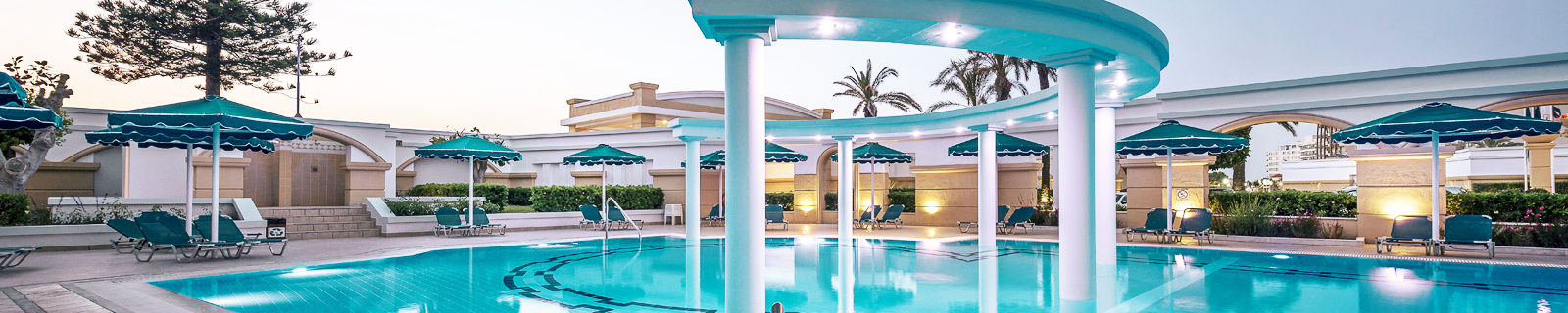 zwembad omringd met blauwe parasols, ligbedjes met pilaren met spots aan een all inclusive hotel